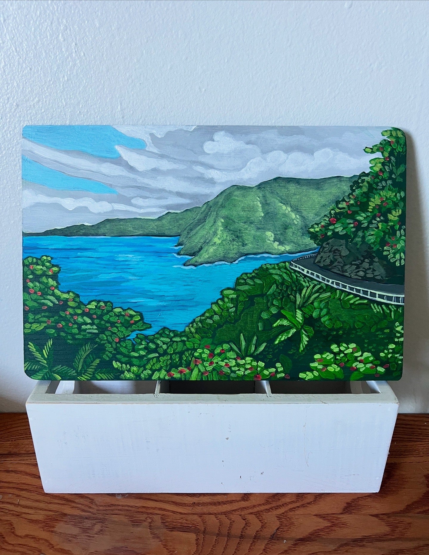 Painting of a scenic landscape with mountains and water on a white stand.